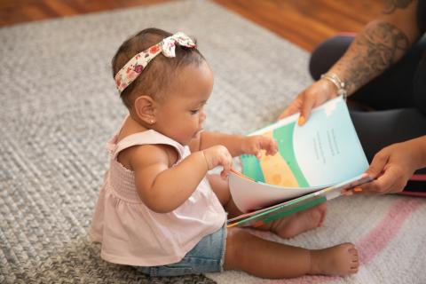 Parent holding book open for baby. 