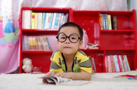 Child looking at viewer with book and a red bookshelf behind him